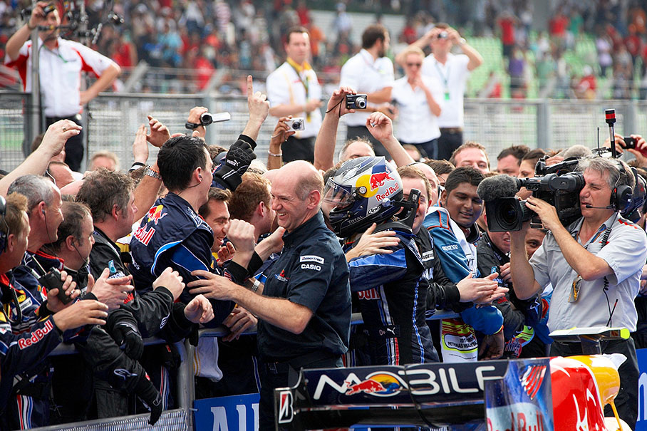 Red Bull chief designer Adrian Newey and race winner Sebastian Vettel enjoy congratulations from the team members at parc ferme fence