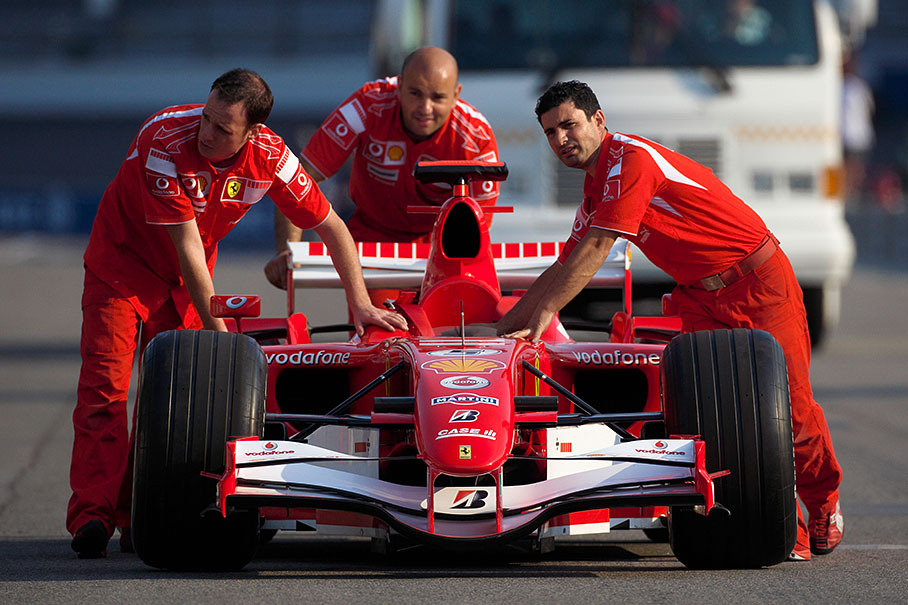 Ferrari mechanics pushing another beautiful lady in red
