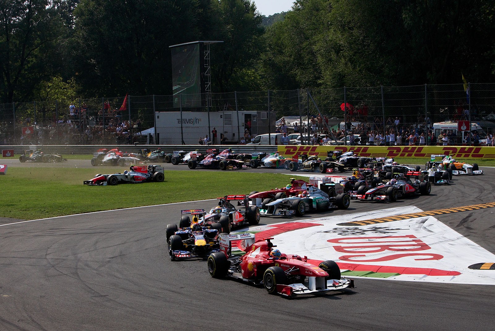 The start field squeezes through turn one with Alonso on Ferrari in the lead and a powerless Liuzzi slides over the lawn, soon crashing into the into the queue