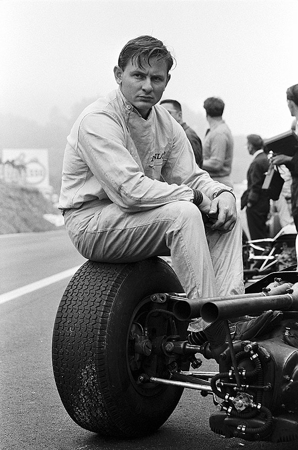 A thoughtful Bruce McLaren sits on a wheel of his Cooper-Climax T77, French GP Clermont-Ferrand 1965
