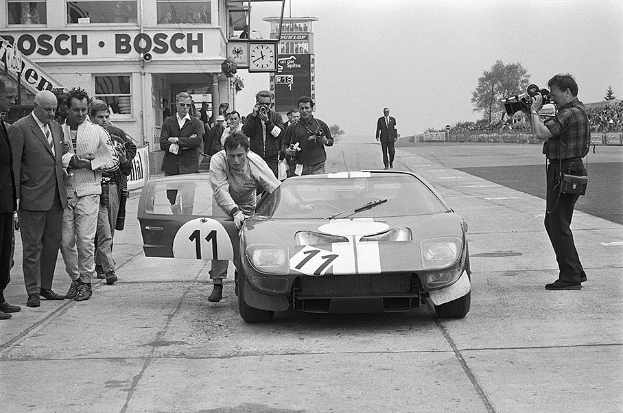 Having missed his refuelling signal, an exhausted Chris Amon pushes the Shelby American Ford GT 40 towards the pits, being watched by officials and photographers, dropping from 3rd to 8th as a result.