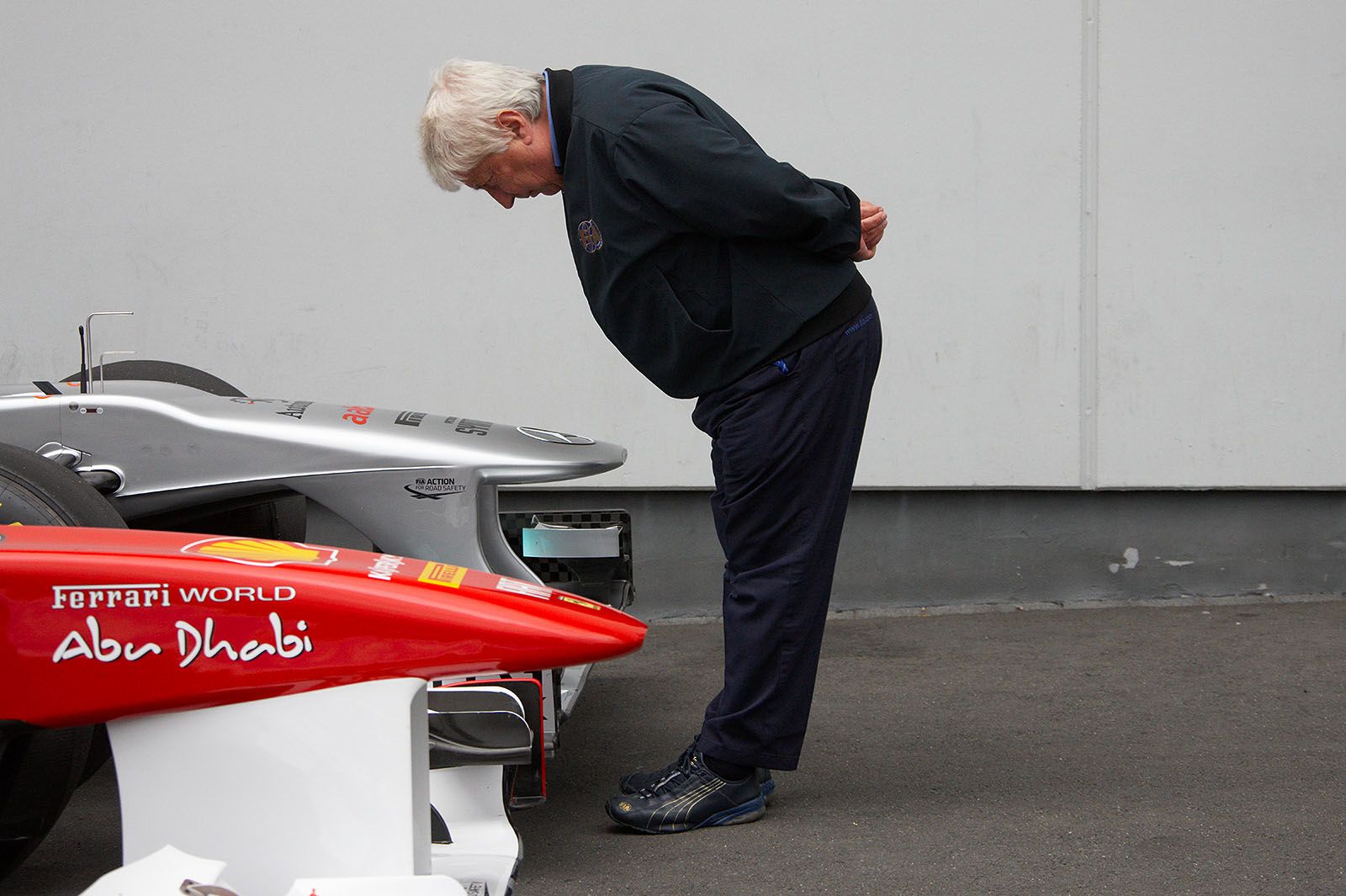FIA's Herbie Blash observes the nose cones of a Mercedes and a Ferrari car after qualifying in parc ferme