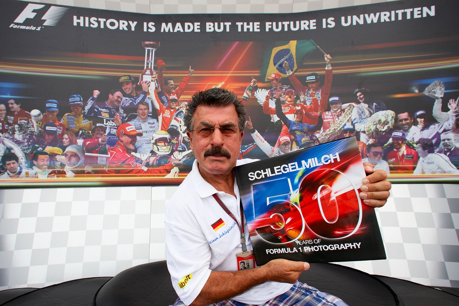 Rainer Schlegelmilch presents the work of his lifetime '50 Years of Formula 1 Photography' on the podium (with some of his portraits on the backdrop)