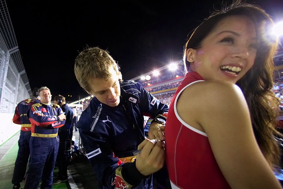 Sebastian Vettel autographs with pleasure a grid girl's ticklish back