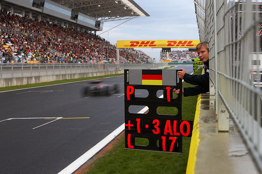 Sebastian Vettel passes the Red Bull pit wall area, his physio Tommi Parmakoski holds the board which still announces first position with 17 laps to go