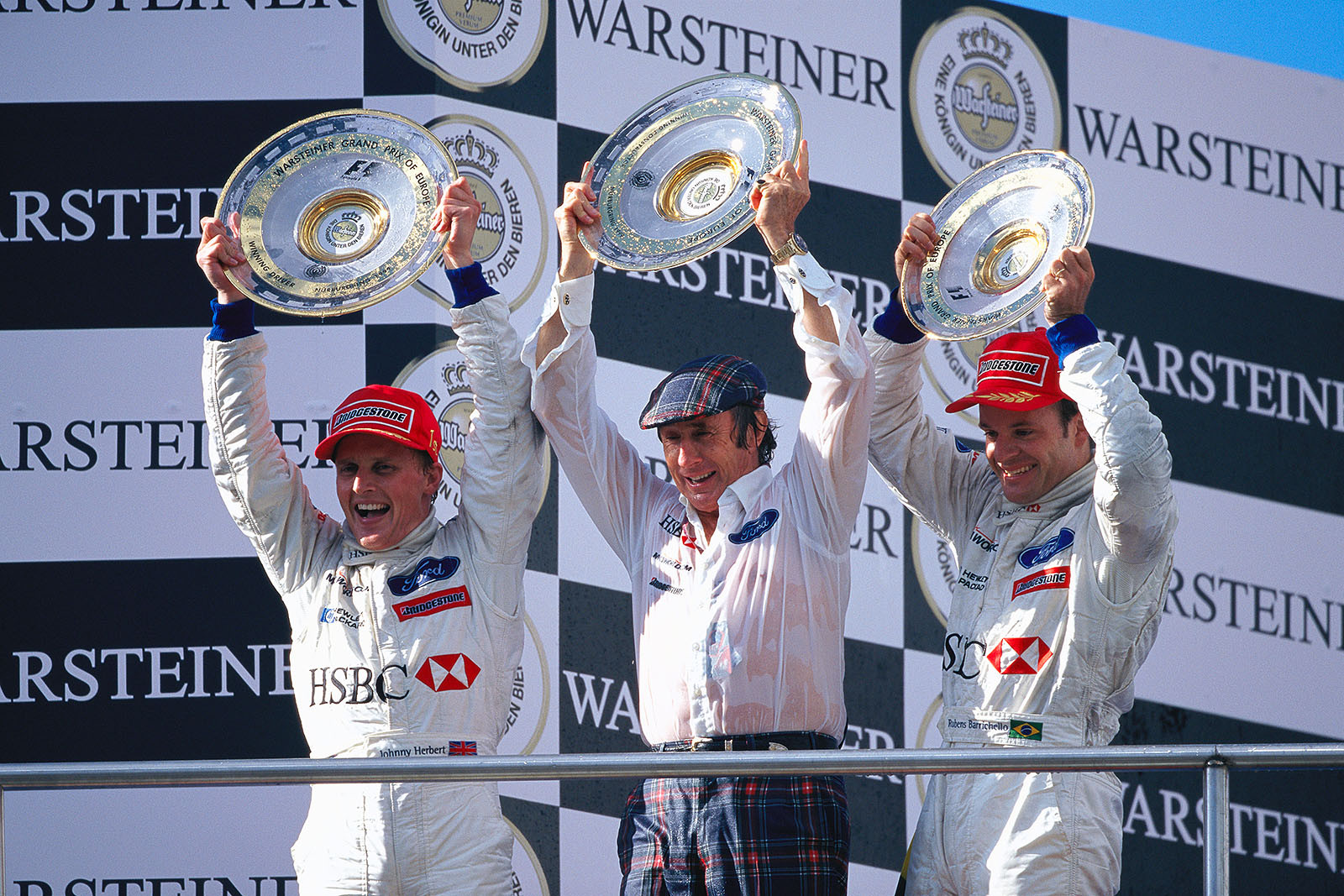 A magnificent victory after a stunning rain race: First placed Johnny Herbert, team boss Jackie Stewart and third placed Rubens Barrichello raise their trophies on the podium of the European Grand Prix at the Nurburgring 1999