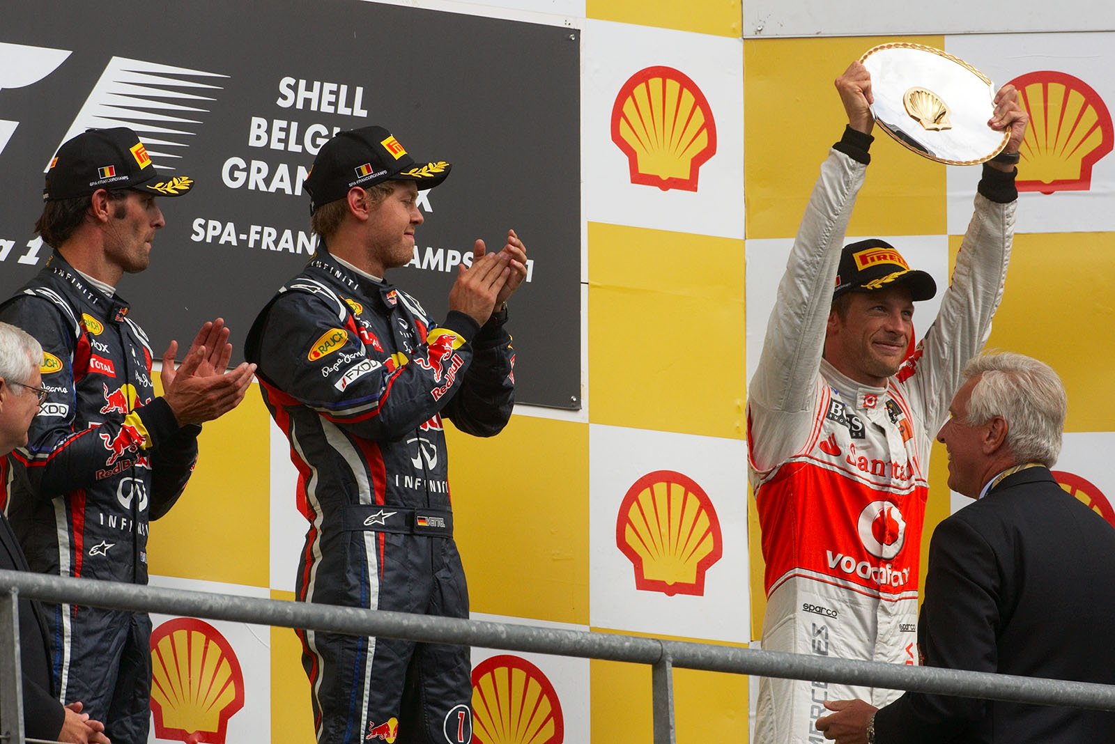 A happy Jenson Button of McLaren raises his trophy for third place on the podium after the Belgian Grand Prix 2011