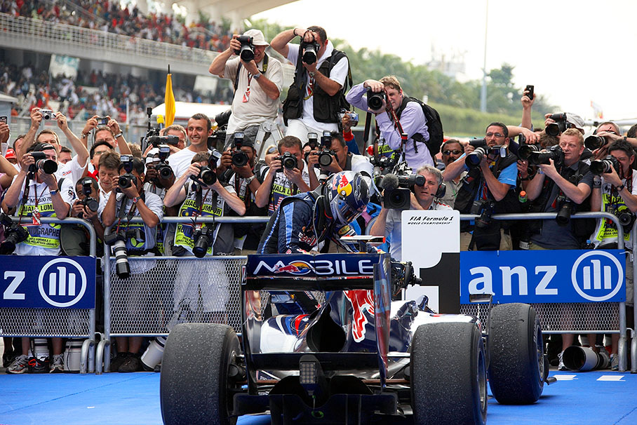 Race winner Sebastian Vettel exits the Red Bull Renault in front of a crowd of pushing photographers around parc ferme