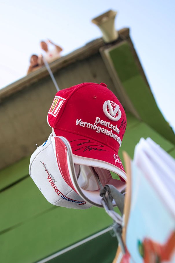 Caps of both Schumachers attached to a rope of an autograph collector, hanging down from a grandstand in to the paddock