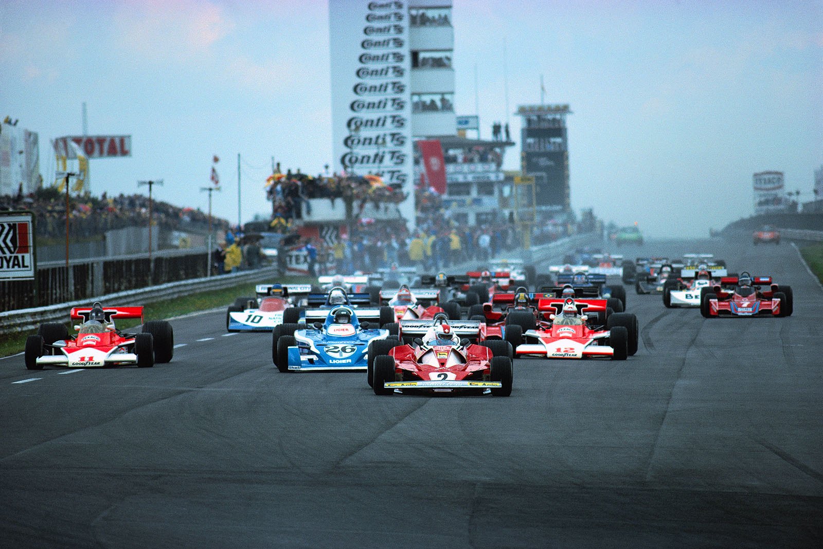 Swiss Ferrari driver Clay Regazzoni has taken the lead at the 1st start for the German Grand Prix 1976. Pole sitter James Hunt (McLaren no. 11) drops back, so as Niki Lauda in the 2nd Ferrari. Jochen Mass in the 2nd McLaren (no. 12) starts on dry weather tyres in the slippery conditions.