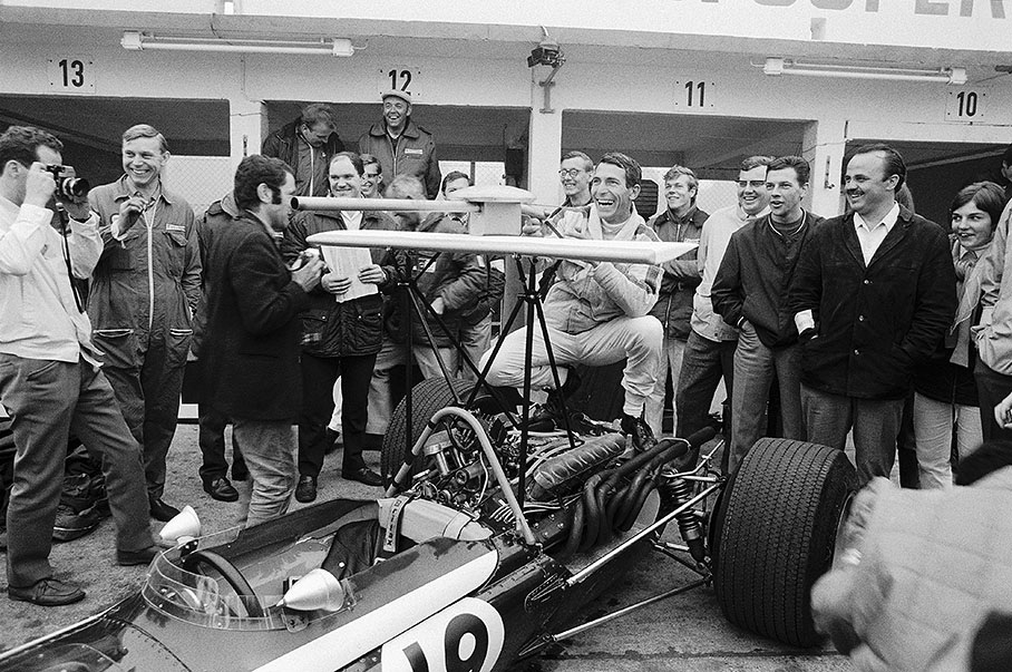 Vic Elford jokes around with Cooper mechanics and journalists sitting on his Cooper-BRM T86B in pits before the German Grand Prix 1968, in which he will retire during the first lap due to an accident