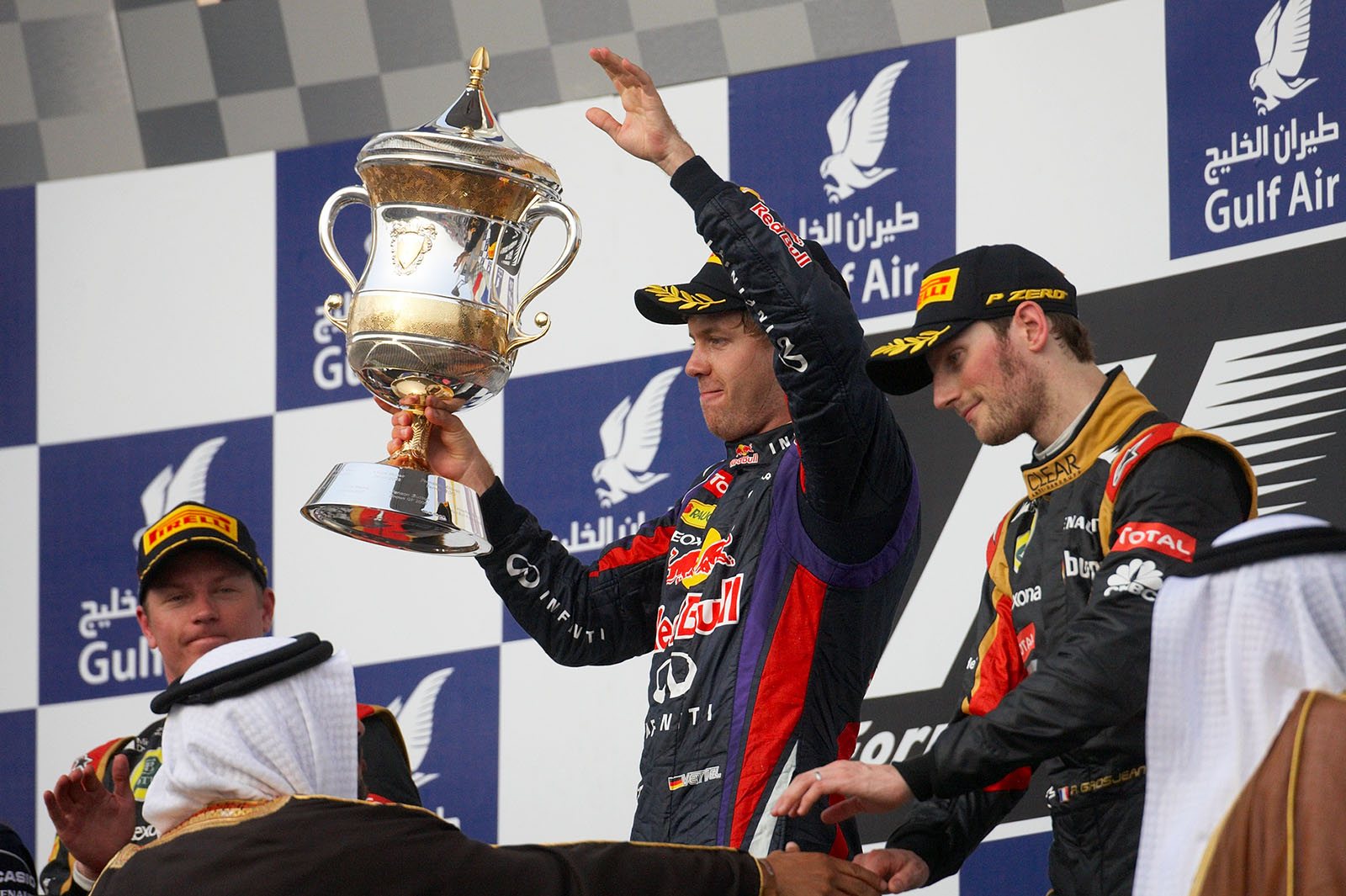 Race winner Sebastian Vettel of Red Bull Racing presents his trophy for the winning driver during the podium ceremony between the second and third placed Lotus race drivers Raikkonen and Grosjean