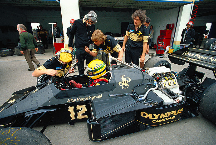 The new Brazilian Lotus driver Ayrton Senna in pits surrounded by mechanics and engineers. Peter Warr (headphones on, without a cap) in the background.