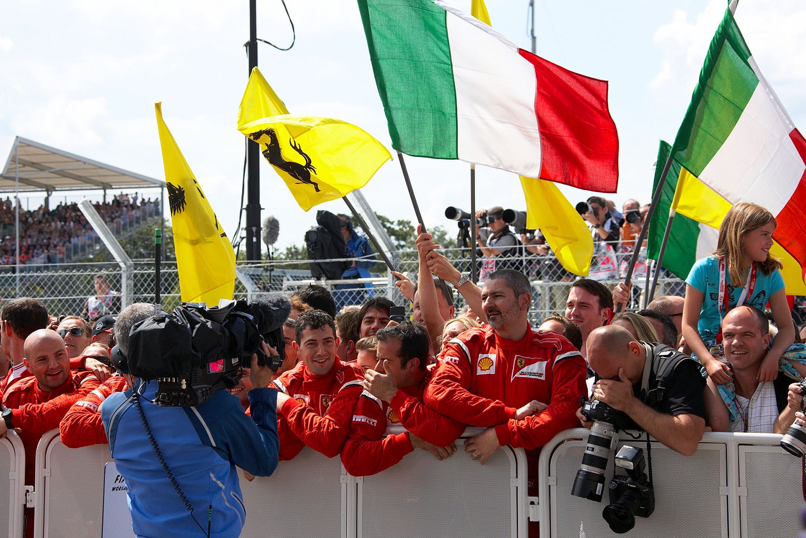 The Ferrari team members cheer and celebrate behind the parc ferme fencing